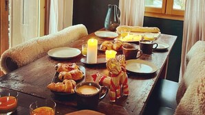Un desayuno acogedor con una mesa de madera, velas, cruasanes y una jarra de jugo de naranja.