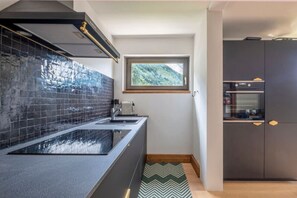 Une cuisine moderne avec un revêtement mural noir, une fenêtre donnant sur les montagnes et des meubles de couleur sombre.