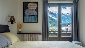 Quarto com cama, radiador, obra de arte emoldurada, janela com vista para montanhas e um cabide.