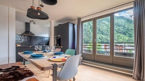 Cozinha moderna com uma janela grande, área de refeições com mesa de madeira e vista para uma montanha arborizada.