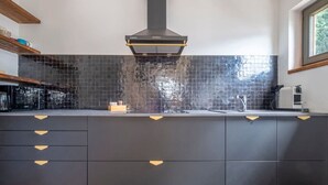 Uma cozinha moderna com armários escuros, painel de azulejos preto e coifa de aço inoxidável.