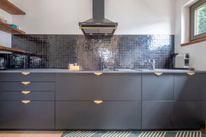 A modern kitchen with dark cabinetry, a black tiled backsplash, and a stainless steel range hood.
