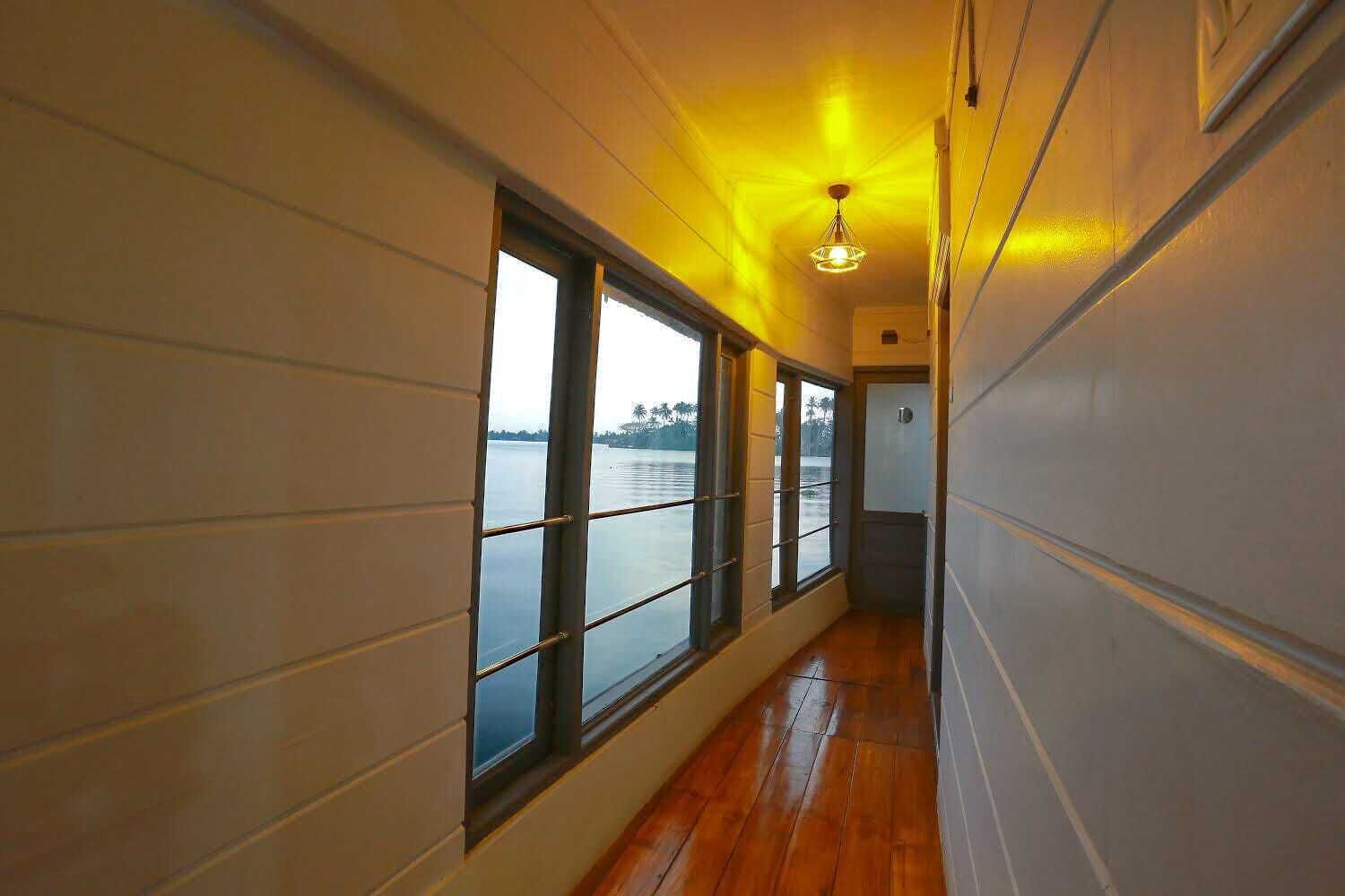 Un couloir doté de grandes fenêtres, d’un plancher en bois et d’un luminaire au plafond.