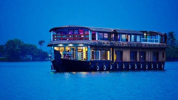 A houseboat with a two-story structure, large windows, and a covered deck area. - Premium Houseboat (Ambalapuzha)