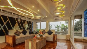 A modern living room with a sectional sofa, a wooden coffee table, and a large window offering a view of greenery. - Premium Houseboat (Ambalapuzha)