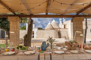 An outdoor dining area with a table set for a meal, a cactus decoration, and a stone building in the background. - Masseria Monte Pizzuto - Le Case di Valentina (Ceglie Messapica)