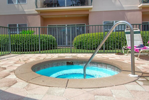 A hot tub with a metal ladder, surrounded by a stone patio, and a metal fence.