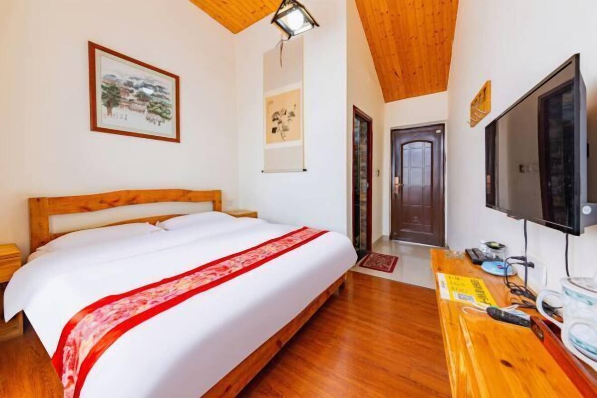 A bedroom with a wooden bed, a flat-screen TV, and artwork on the walls.