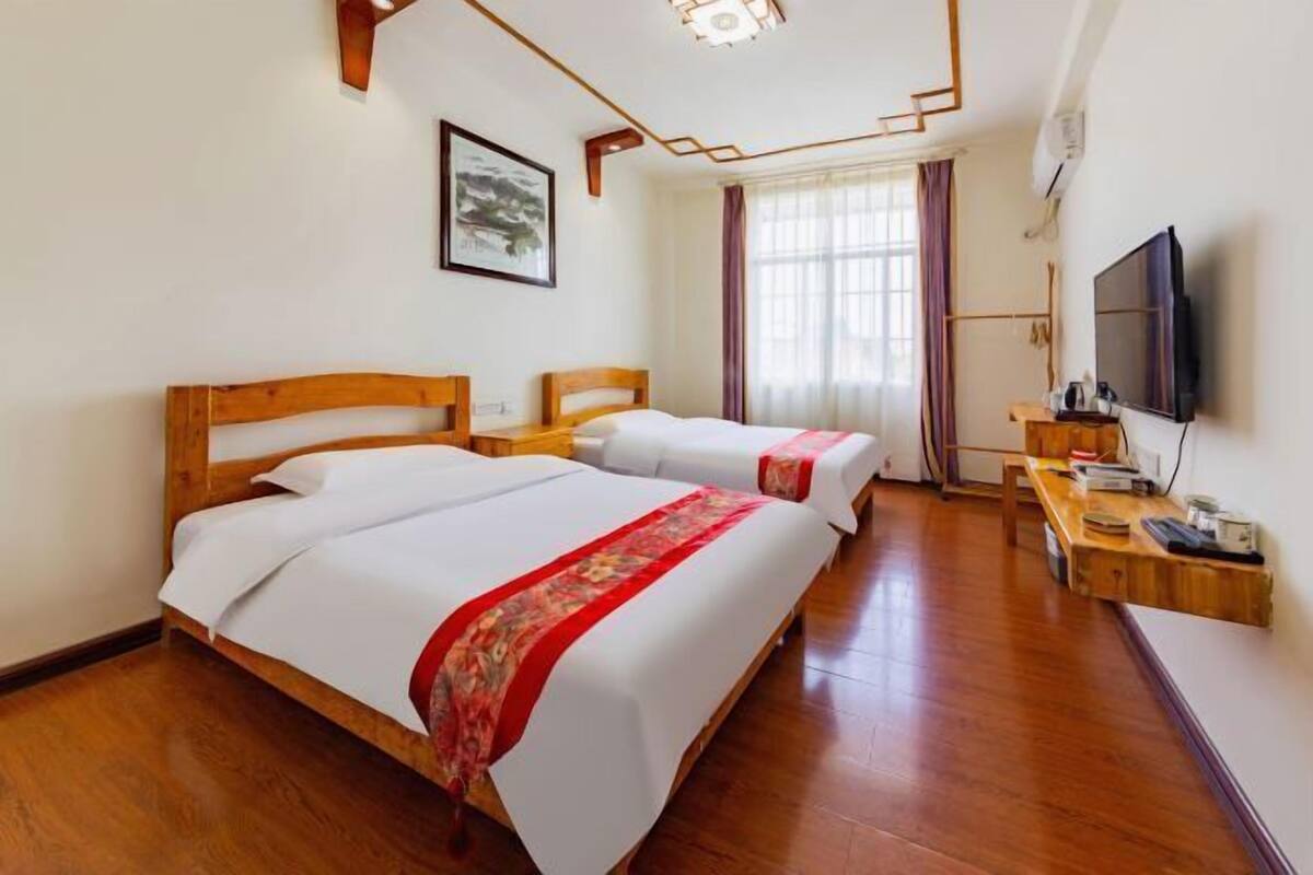 A hotel room with two wooden beds, a television, and a desk with a chair.