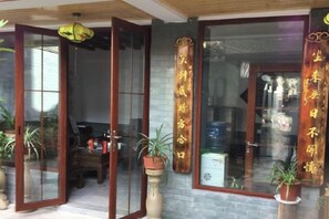 A traditional Chinese-style entrance with sliding glass doors, a stone wall, and potted plants. - Han Shu Xiang Yuan Hostel (Jianshui)