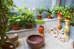 Un patio con plantas en macetas, un gran cuenco de terracota y un banco de piedra.