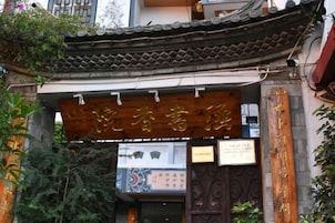 Um portão chinês tradicional com letras douradas, dando acesso a um edifício com telhado em telhas.