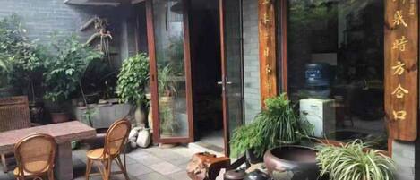 Un espacio al aire libre con mobiliario de mimbre, plantas en macetas y una mesa de madera.