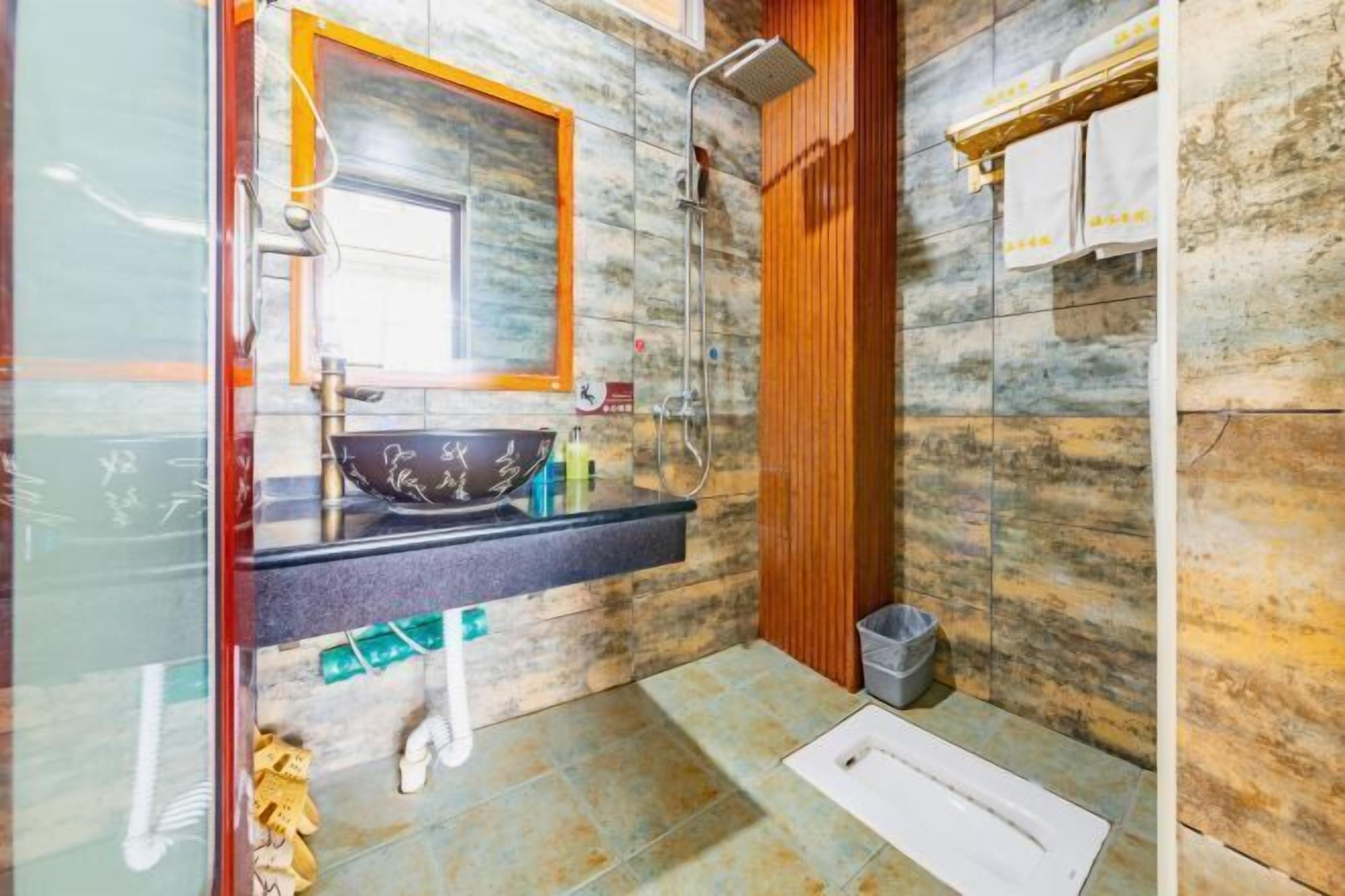 A bathroom with a marble wall, a wooden vanity, a sink with a decorative bowl, a shower, and a toilet.