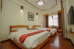 Quarto de hotel com duas camas de madeira, luminária no teto, quadro pendurado na parede e televisão ao lado direito.