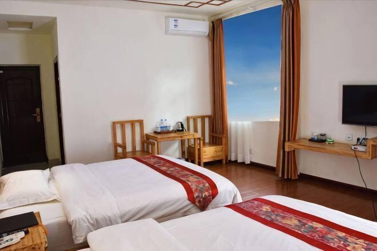 A hotel room with two beds, a desk, a chair, a television, and a window with curtains.