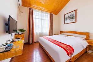 Quarto de hotel com teto de madeira, cama com corredor decorativo vermelho, televisão sobre uma escrivaninha de madeira e um quadro na parede.