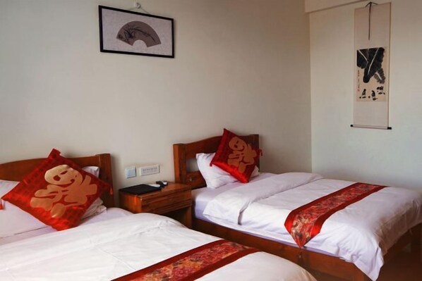 Habitación de hotel con dos camas, cada una con ropa de cama blanca y almohadones decorativos rojos. Hay una obra de arte enmarcada en la pared sobre las camas y un pergamino colgante a la derecha.