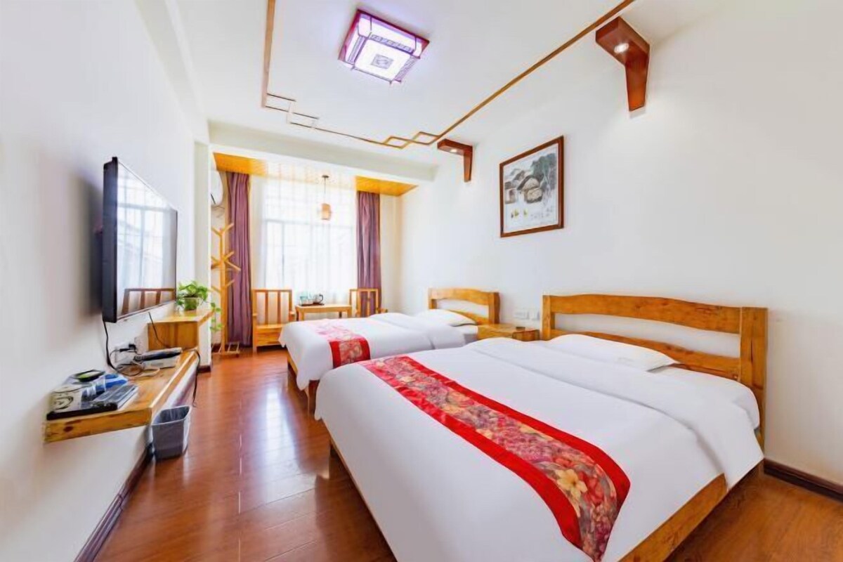 Quarto de hotel com duas camas, televisão, escrivaninha e janela com cortinas.