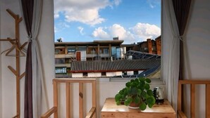 En balkon med udsigt til traditionelle bygninger, et træbord med en potteplante og en elkedel.