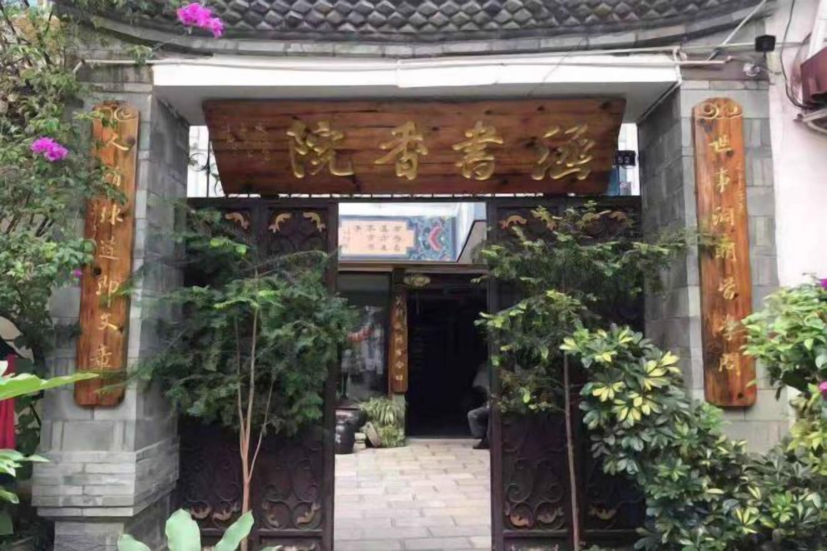 Um portão tradicional chinês com caracteres chineses, dando acesso a um edifício com telhado de telhas.