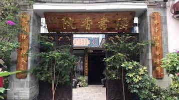 Um portão tradicional chinês com caracteres chineses, dando acesso a um edifício com telhado de telhas.