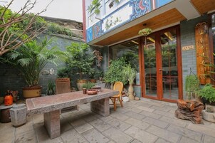 Un patio con una mesa y sillas de piedra, rodeado de plantas en macetas y un banco de madera.