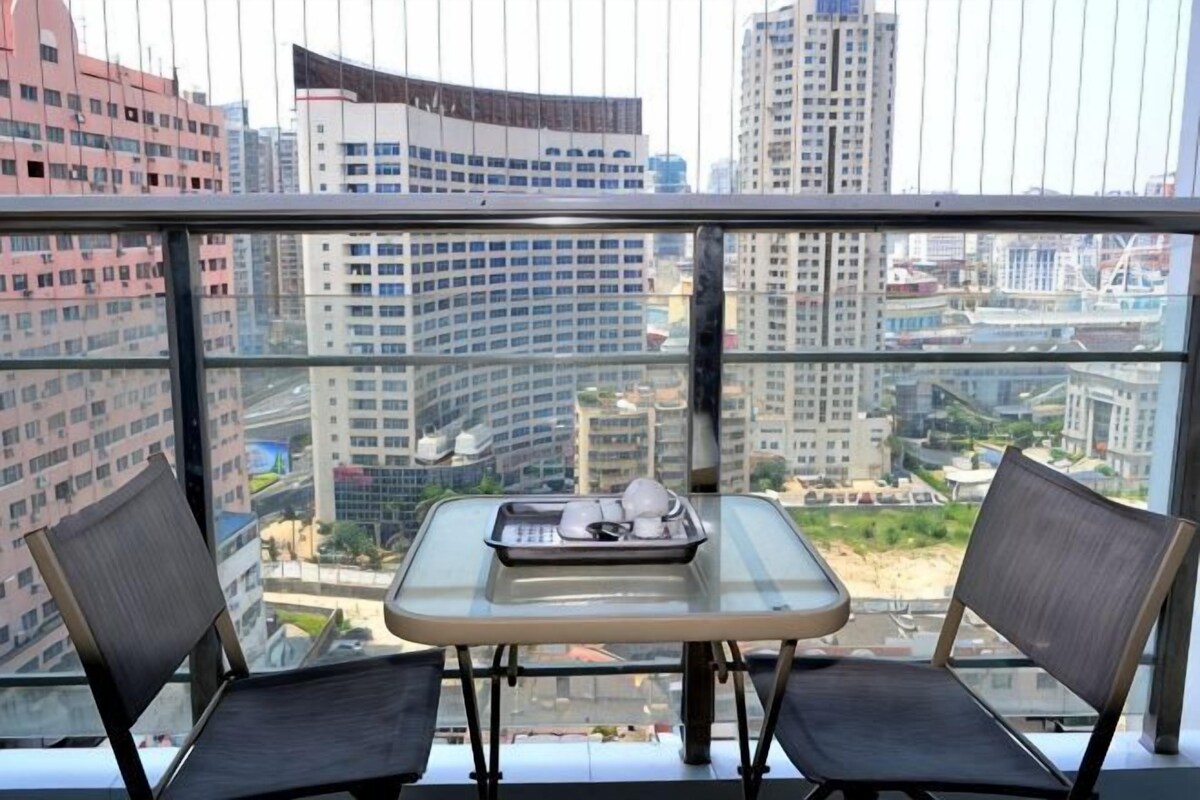 A balcony with a table and two chairs, overlooking a cityscape with high-rise buildings.