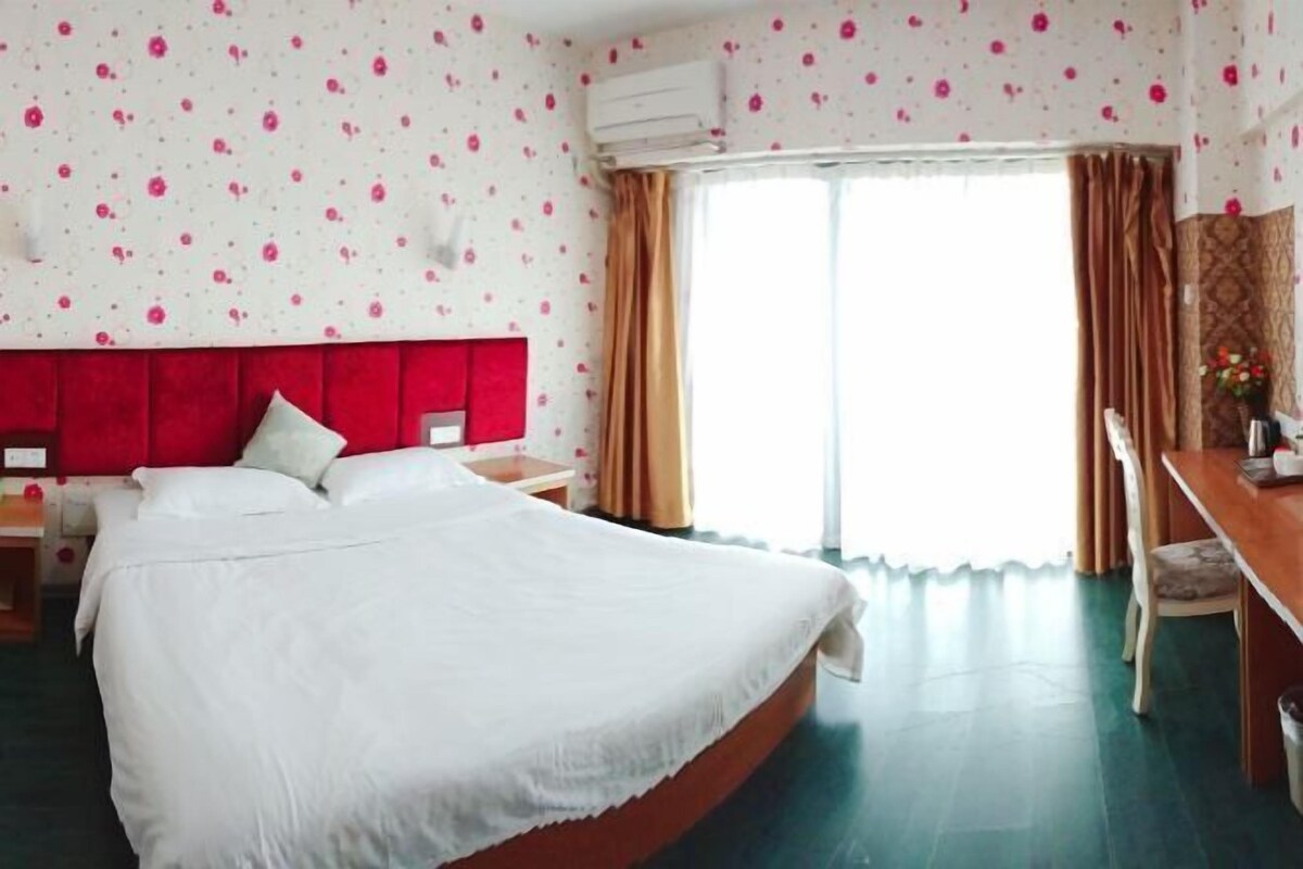 A hotel room with a bed, a desk, and a chair. There is a window with curtains.