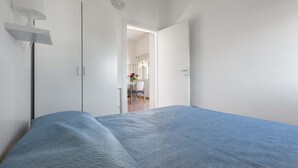 Un dormitorio con una cama, una lámpara de noche y una puerta que da a otra habitación.