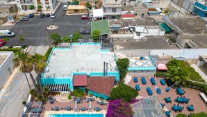 Vista aérea de un hotel con piscina, mobiliario exterior y terraza en la azotea.