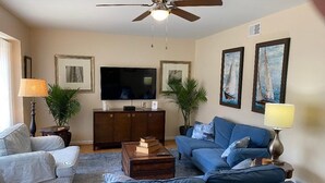 Ein Wohnzimmer mit Deckenventilator, Fernseher, Sofa, Couchtisch und zwei Nachttische mit Lampen.