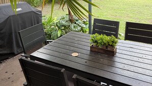 Eine Terrasses mit gedecktem Tisch und Stühlen, umgeben von Grün und Blick auf einen Garten.