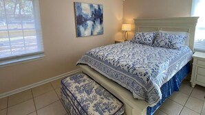 Ein Schlafzimmer mit einem Bett, einem Deckenventilator, einem Nachttisch, einer Lampe, einem Fenster und einem Gemälde.