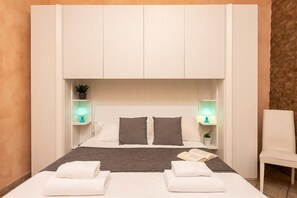 Une chambre d’hôtel avec un lit, deux tables de chevet avec des lampes, une chaise et une petite plante.