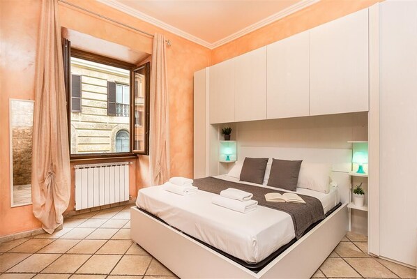 Une chambre à coucher avec un lit, des lampes de chevet, une fenêtre et une vue sur un bâtiment à l’extérieur.