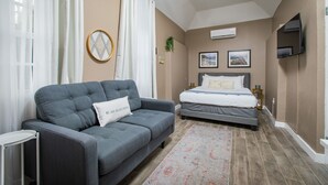 Een slaapkamer met een grijze bank, een bed, een aan de muur bevestigde televisie en een plafondventilator.