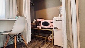 Een kleine kamer met een bureau, stoel en een klein keukentje.