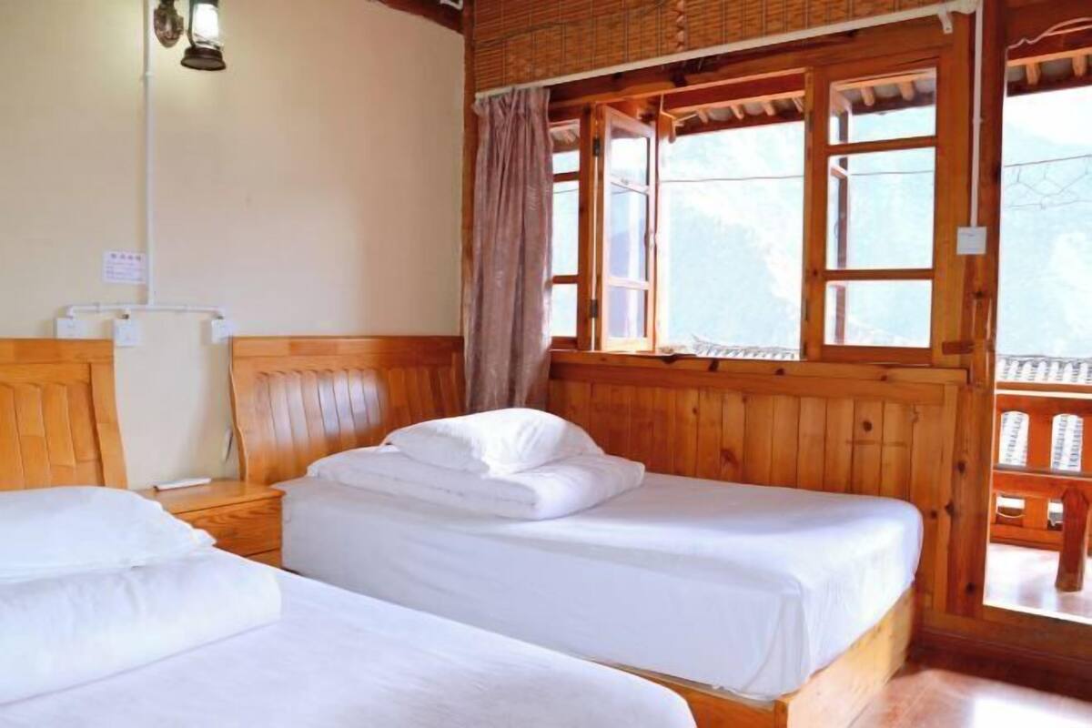 Una habitación con dos camas, paredes de madera, un ventanal con cortinas y un termostato a la vista en la pared.