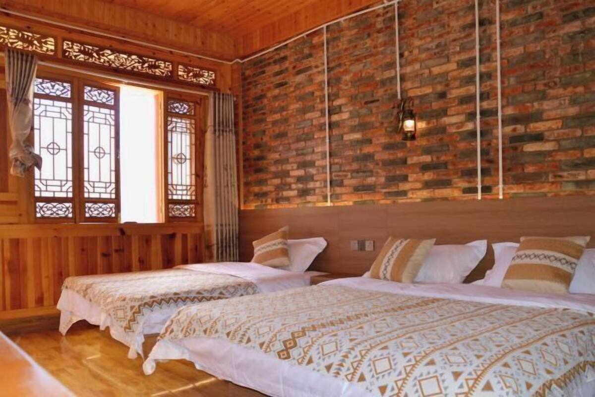 Habitación con dos camas, paredes de madera y un muro de ladrillo decorativo, además de un farol colgante.