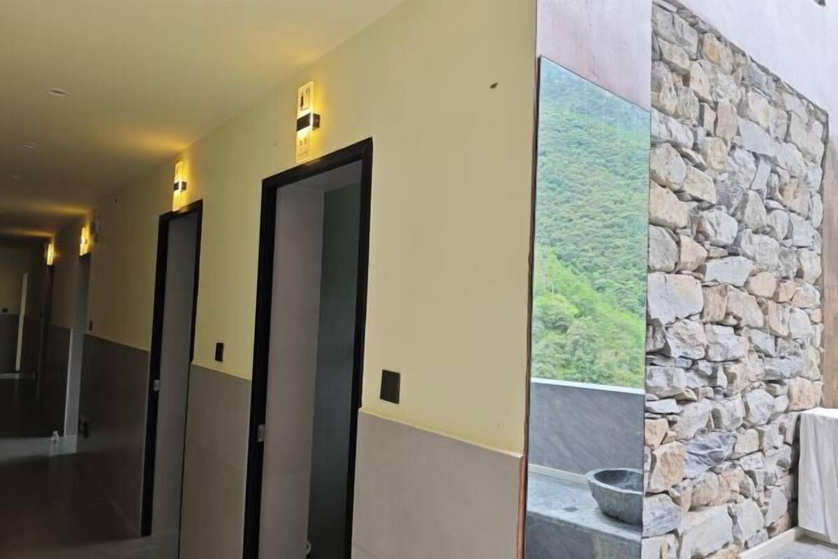 Un pasillo con puertas, un muro de piedra y vista a vegetación.