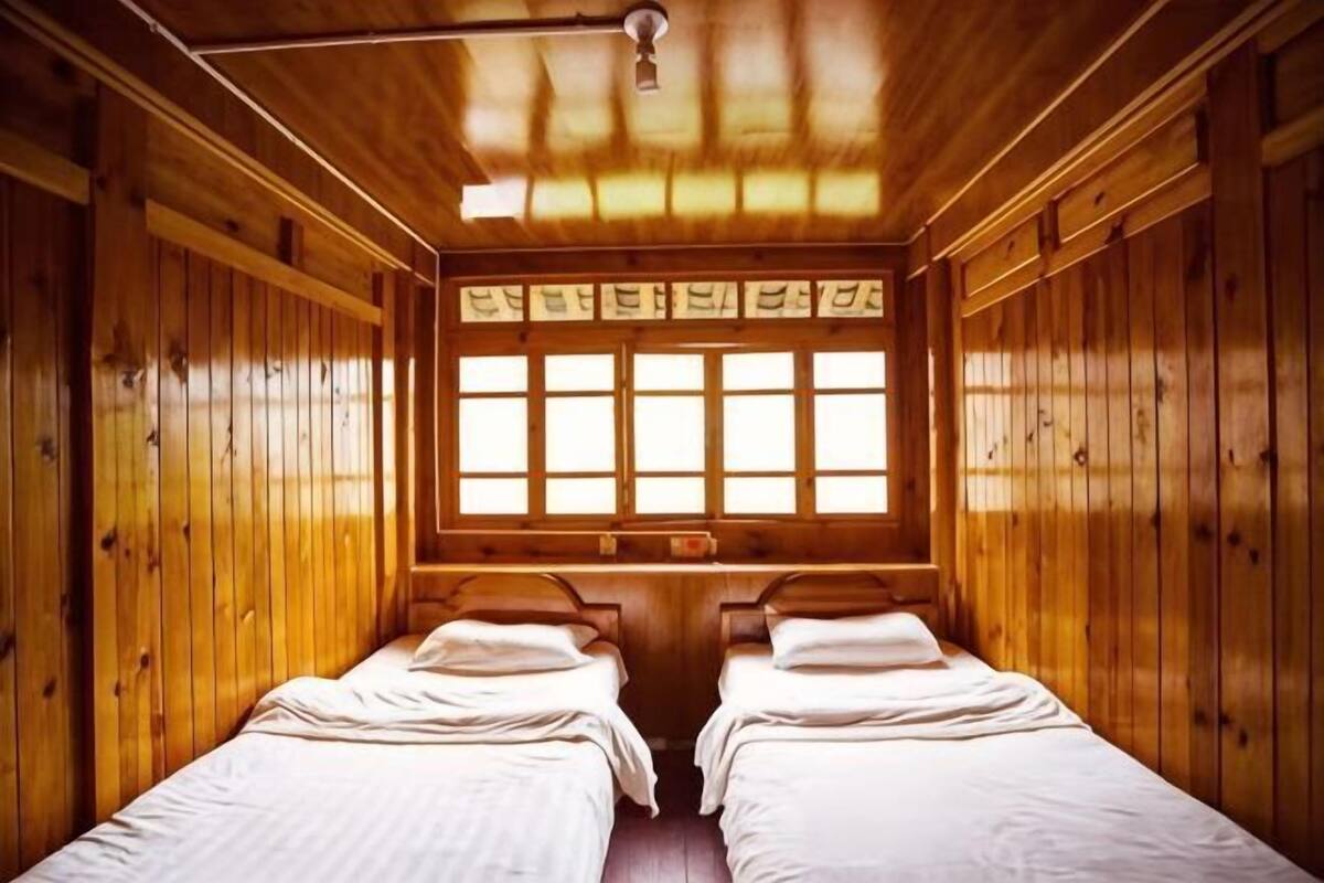 Una habitación tipo cabaña de madera con dos camas, un ventanal grande y una lámpara en el techo.
