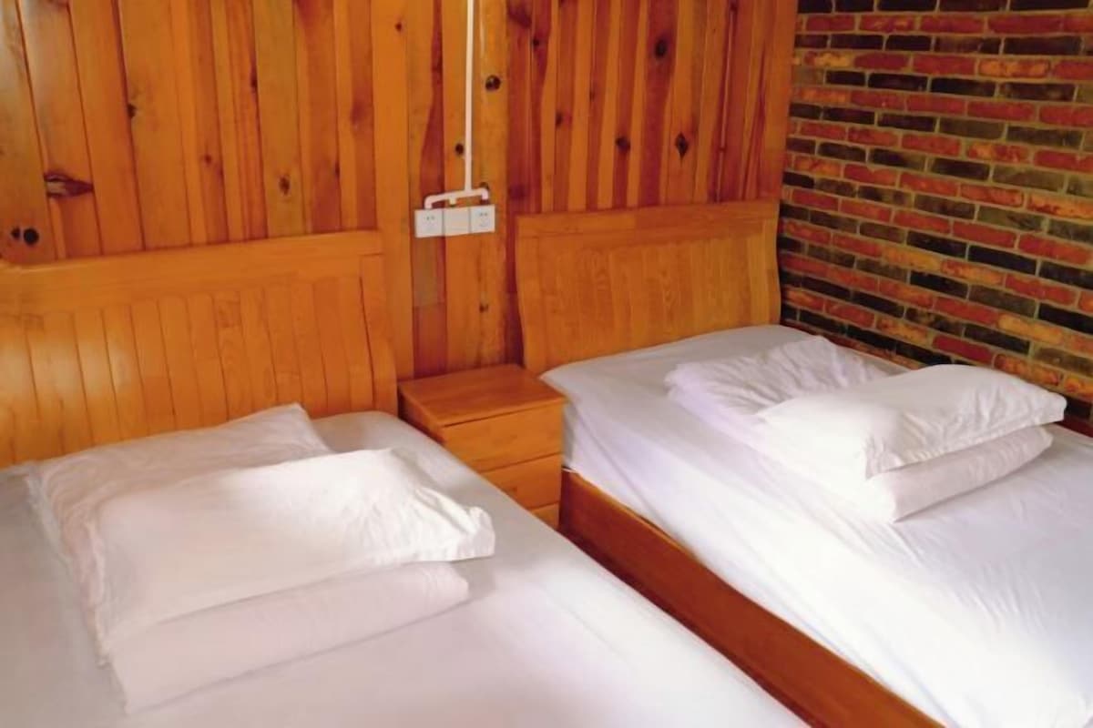Une chambre avec deux lits, des têtes de lit en bois, un mur en briques et une petite table de chevet en bois.