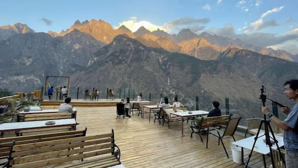 Una terraza con mesas y bancos de madera que da a un paisaje montañoso.