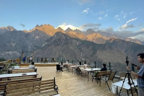 A terrace with wooden tables and benches overlooking a mountainous landscape. - Tiger Leaping Gorge Tea-Horse Guesthouse (Shangri-La)