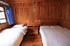 Een houten hutje met twee bedden, een klein tafeltje en een raam met gordijnen.