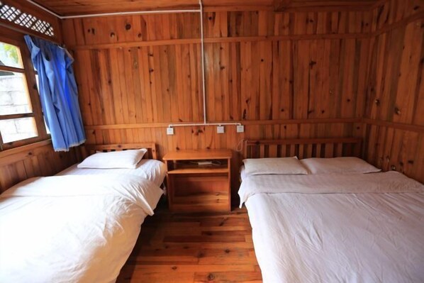 Una cabaña de madera con dos camas, una mesita y un ventanal con cortinas.