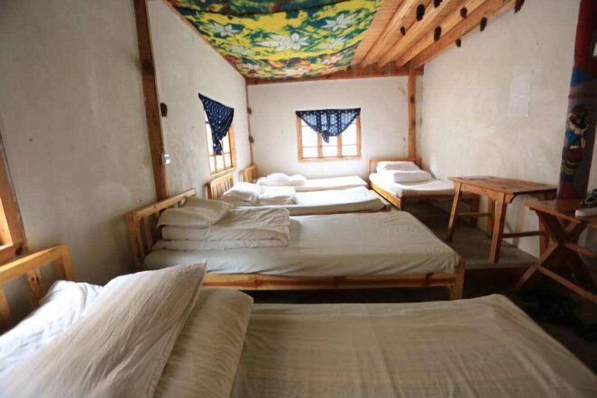Una habitación con tres camas de madera, una mesita pequeña y una ventana con cortina.