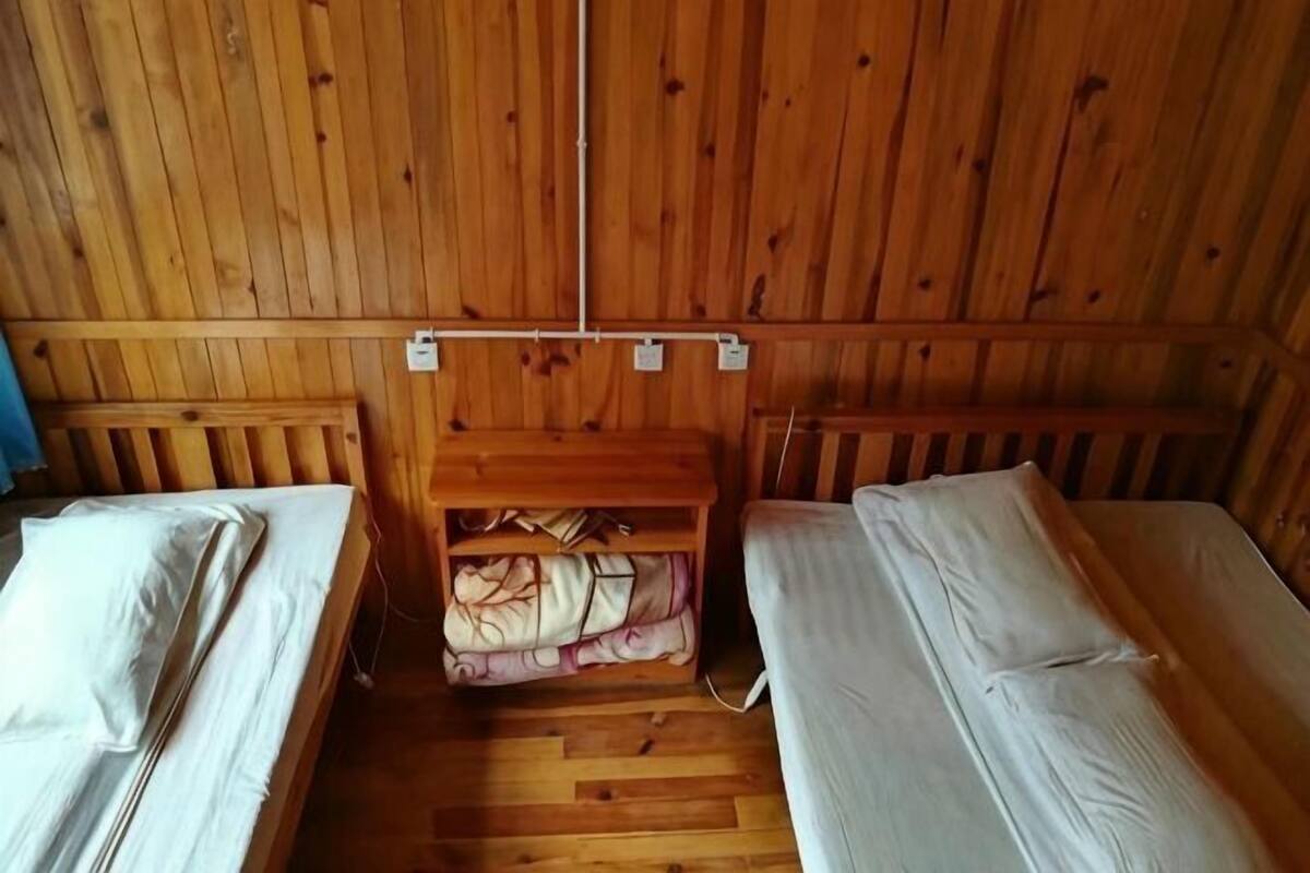 Una cabaña de madera con dos camas individuales, un estante con mantas y una pared de madera con toma de corriente.
