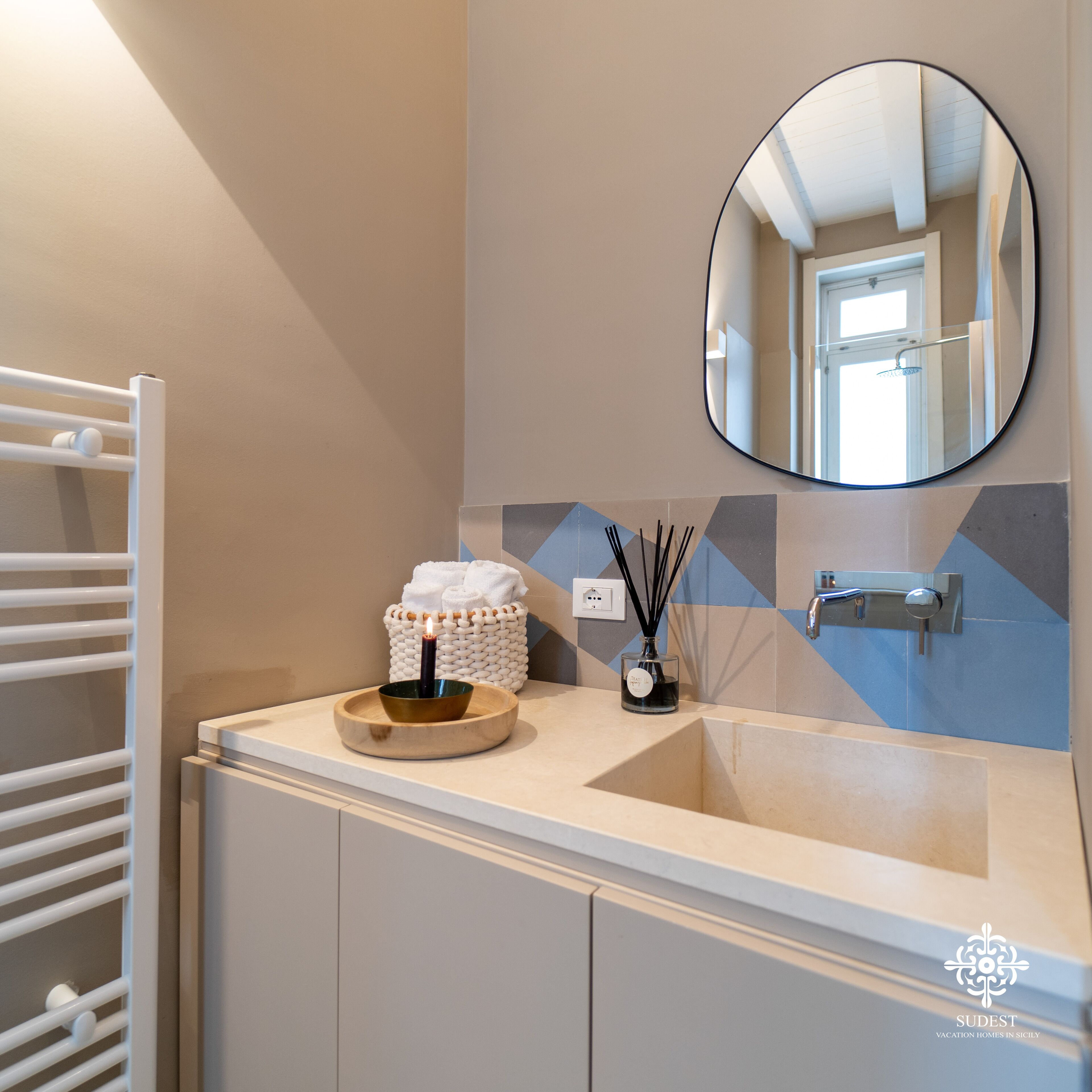 Un baño con un lavamanos blanco, un espejo redondo, un perchero para toallas y un candelabro decorativo.
